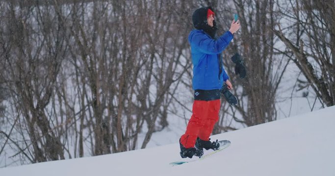 Male snowboarder rides the Board at the ski to the snow slope and writing messages to smartphone to your friends