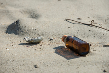 An empty brown clear bottle with cap left trashed on the beach. A starting point of the environment problem.