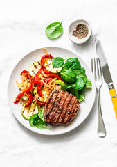 Beef steak with grilled  vegetables, sweet pepper, zucchini and fresh spinach on a light background, top view. Delicious healthy balanced lunch