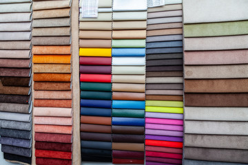 Pieces of leather and textile material for interior trim and furniture making for example in the catalog of different colors for the design studio. Many colored materials hanging on the wall in stock.