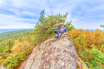 A mature tourist rests on the top of a cliff.