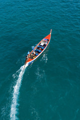 View from above, aerial view of a beautiful long tail boat that sails on a blue sea leaving behind a long wake of water. Phuket, Thailand.