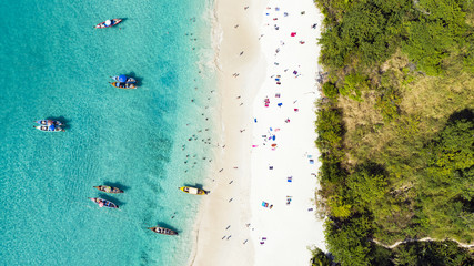 View from above, aerial view of a beautiful tropical beach with white sand and turquoise clear water, long tail boats and people sunbathing, Freedom beach, Phuket, Thailand.