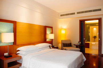 Vintage white cozy hotel bedroom with classic wooden bed, lamp and pillows