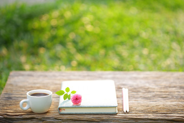 White coffee cup and notebook with pink pygmy rose on wooden table