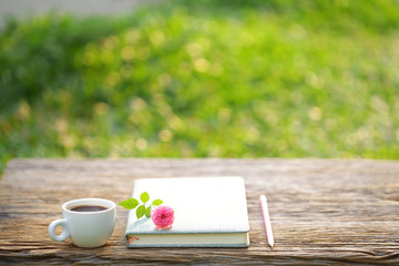White coffee cup and notebook with pink pygmy rose on wooden table