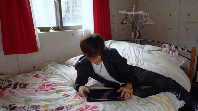 Stylish Japanese Man Using Tablet Computer in Bed