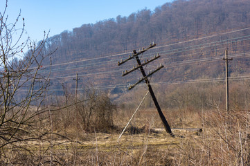 The falling electric pole in the field with the dried grass and prickly bushes. The inclined pole...