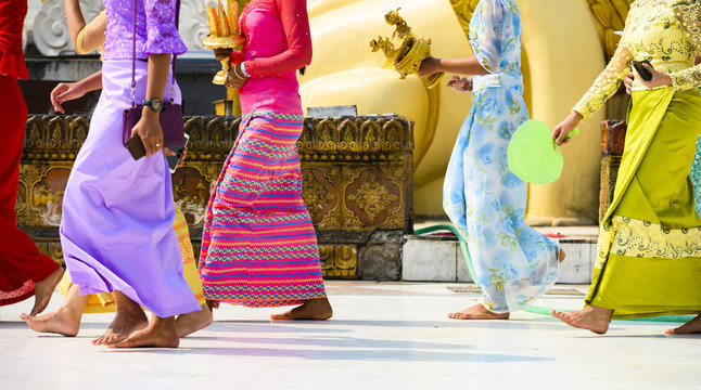 (selective focus) Some Burmese Buddhist faithful are walking barefoot around the Shwedagon Pagoda wearing a traditional and colorful Longyi (traditional Burmese clothes). Yangon, Myanmar.