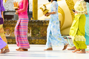 Fototapeta premium (selective focus) Some Burmese Buddhist faithful are walking barefoot around the Shwedagon Pagoda wearing a traditional and colorful Longyi (traditional Burmese clothes). Yangon, Myanmar.