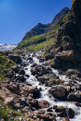 The river flows among the stones from the mountain in the surroundings of Dombai. The Caucasus Mountains on a summer, clear day. Tourie Lake.