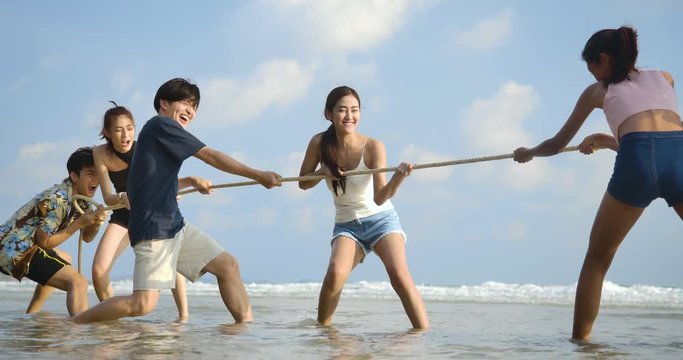 Group of Young People Having Fun on the Beach. Smiling friends playing tug of war at beach on a sunny day. People with party celebration concept. 4K resolution. Slow motion shot.