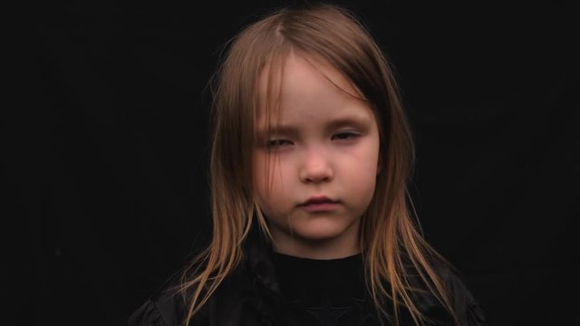 Close-up portrait of a serious sad cute little girl in black clothes
