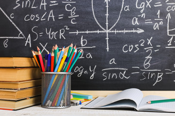 School desk in classroom, with books on background of chalk board with written formulas. Soncept Teacher's Day.