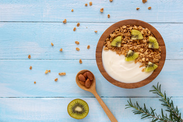 Top view of yogurt in a wooden bowl with granola,fresh kiwi, mint and  spoon on blue wooden table. Health food concept.