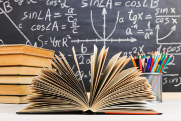 School desk in classroom, with books on background of chalk board with written formulas. Soncept Teacher's Day.