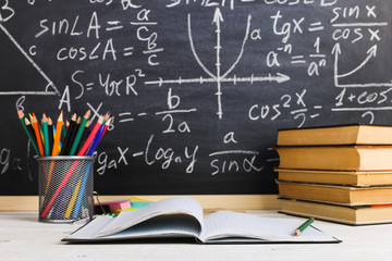 School desk in classroom, with books on background of chalk board with written formulas. Soncept Teacher's Day.