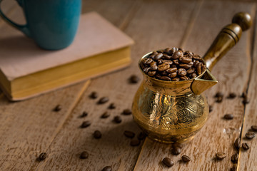 fresh roasted coffe beans in  cezve (traditional turkish coffee pot) closed book and cup on wooden table.