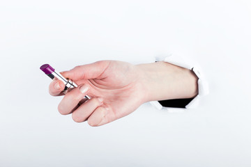 Female hand out of a hole in paper, holds open lipstick. Isolate on white background.