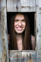 Young woman looks from the little window of a wooden barn.