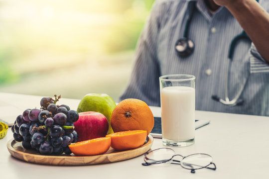 Senior Male Nutritionist Doctor Working On Desk With Healthy Food Fruits And Milk On Table In The Hospital Office. Dieting And Well Eating Menu Concept.