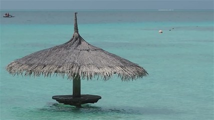 Straw umbrella in the water, free space on the right. Resort on a tropical island