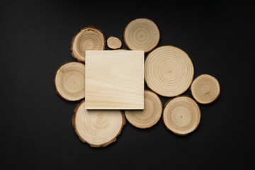 Pine tree cross-sections with annual rings and wooden square on black background. Lumber piece close-up shot, top view.