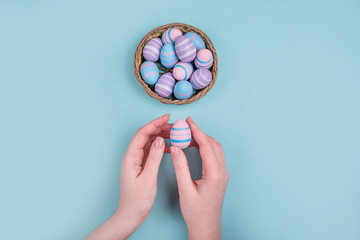 Woman hands holding dyed on blue, pink and violet Easter eggs in the straw basket isolated on blue...