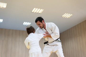 Young judoka and his father engaged in judo class in a dojo. Trainer teaches child the methods and positions of single combat, judo, karate or aikido
