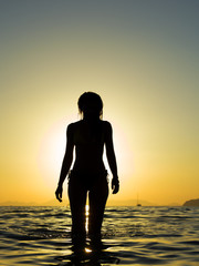 young woman walking in the sea at sunset