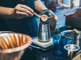 Barista's hand putting ground coffee in stainless steel coffee grinder