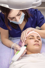 Obraz na płótnie Canvas Cosmetologist performs phonophoresis procedure for the skin of beautiful, young woman in beauty salon. Cosmetology and professional skin care.
