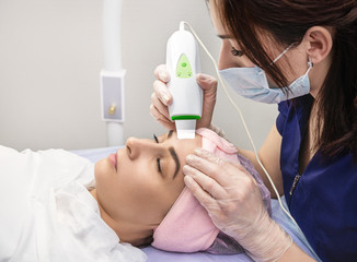 Cosmetologist performs phonophoresis procedure for the skin of  beautiful, young woman in beauty...