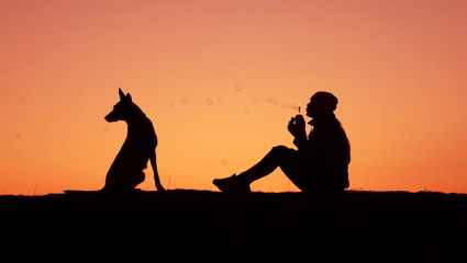 Silhouettes girl and dog at sunset, girl blows bubbles, incredible sunset, Belgian Shepherd Malinois
