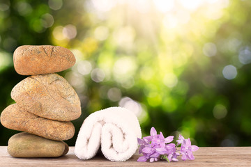 Stack of stone and white towel with flower on wooden floor on green bokeh background, spa concept