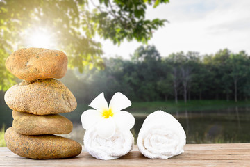 Stack of stone and white towel with white flower on wooden floor on green nature background, spa concept