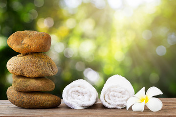 Fototapeta na wymiar Stack of stone and white towel with flower on wooden floor on green bokeh background, spa concept