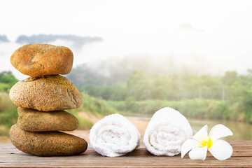 Stack of stone and white towel with white flower on wooden floor on nature background, spa concept