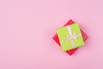 Two gift boxes wrapped in color green and red polka dots paper and tied with pink and craft ribbon on pink background. Top view, gift idea for him and her. Copy space. Mother's day woman's day concept