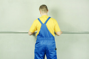 Builder in work clothes against a gray wall, leveling the wall. A man carefully corrects...