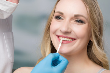 Using shade guide at womans mouth to check veneer of tooth