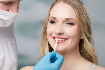 dentist using shade guide at womans mouth to check veneer of tooth