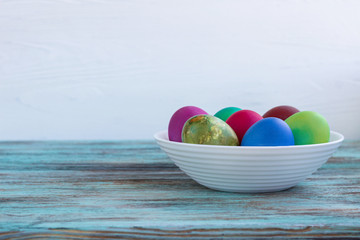 White plate of Easter multicolored eggs on wooden background