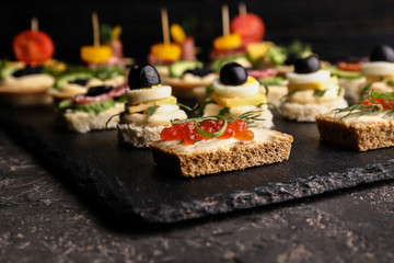 Slate plate with tasty canapes on dark table, closeup