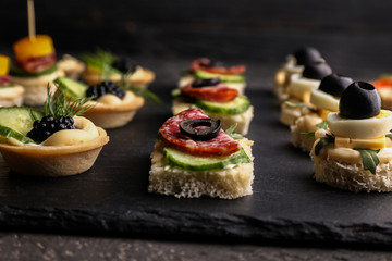 Slate plate with tasty canapes on dark table, closeup