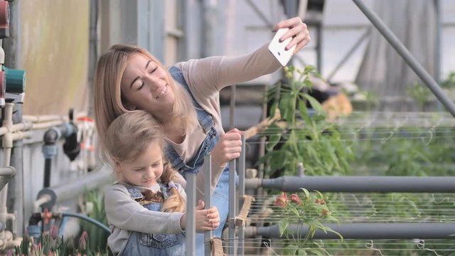 A woman with a small daughter take a selfie in a greenhouse with flowers in spring.