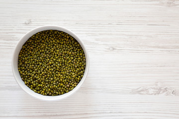 Raw green mung beans in a gray bowl over white wooden surface, top view. Flat lay, overhead, from above. Copy space.