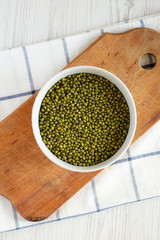 Full bowl of green mung beans on rustic wooden board over white wooden background. Flat lay, overhead, from above.