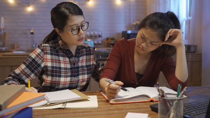 Obraz premium Group of asian friends studying with laptop and books together and worried with final exams roommate comfort her. young college girls stay up late at home night kitchen in dark room indoors.
