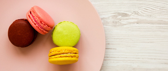 Colorful macarons on a pink plate over white wooden background, top view. Copy space.